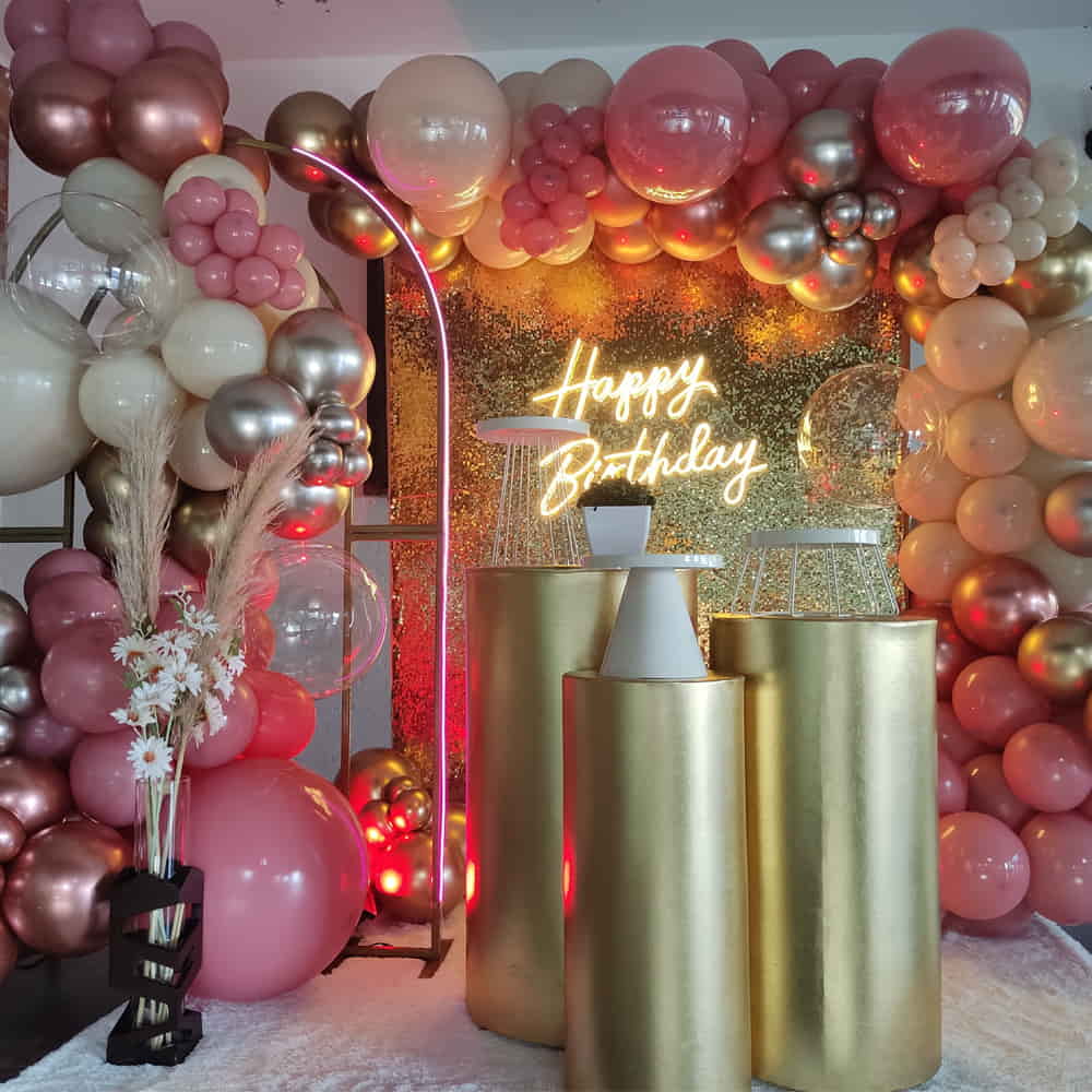 Decoración de cumpleaños con centro de mesa dorados y un espectacular arco y bombas rosas con crema y dorado