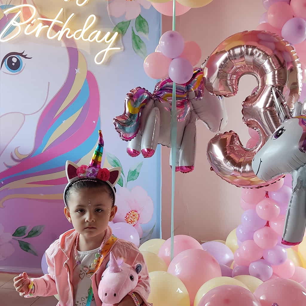 Gran decoración de cumpleaños con bombas color pasteles y unicornios con una hermosa niña